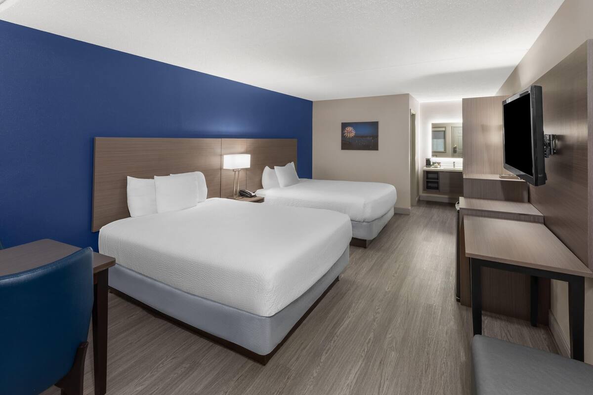 A hotel room with two beds, a desk, a chair, a TV, and a bathroom visible in the background.