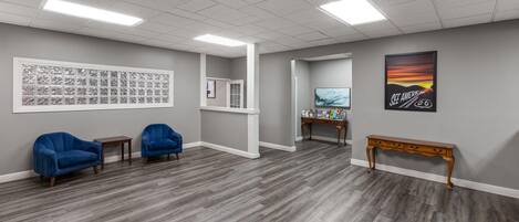 A room with grey walls, a large window, two blue chairs, a wooden bench, and a framed picture on the wall.