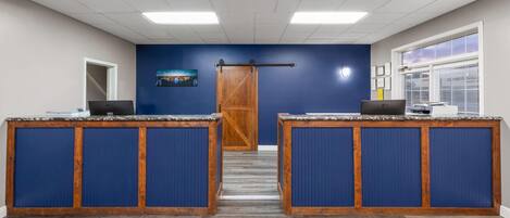 A reception area with two desks, a wooden door, a blue wall, and a window with blinds.
