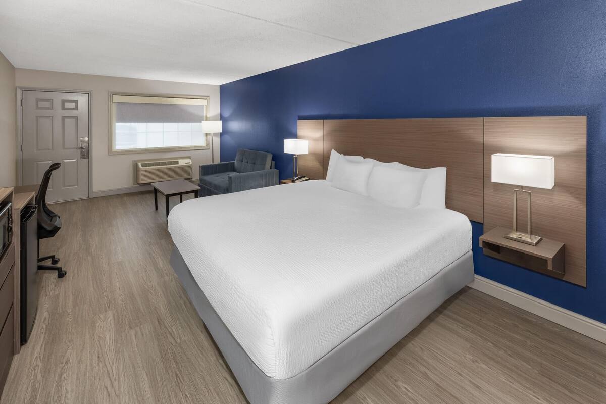 A hotel room with a large bed, a desk, a chair, and a window.