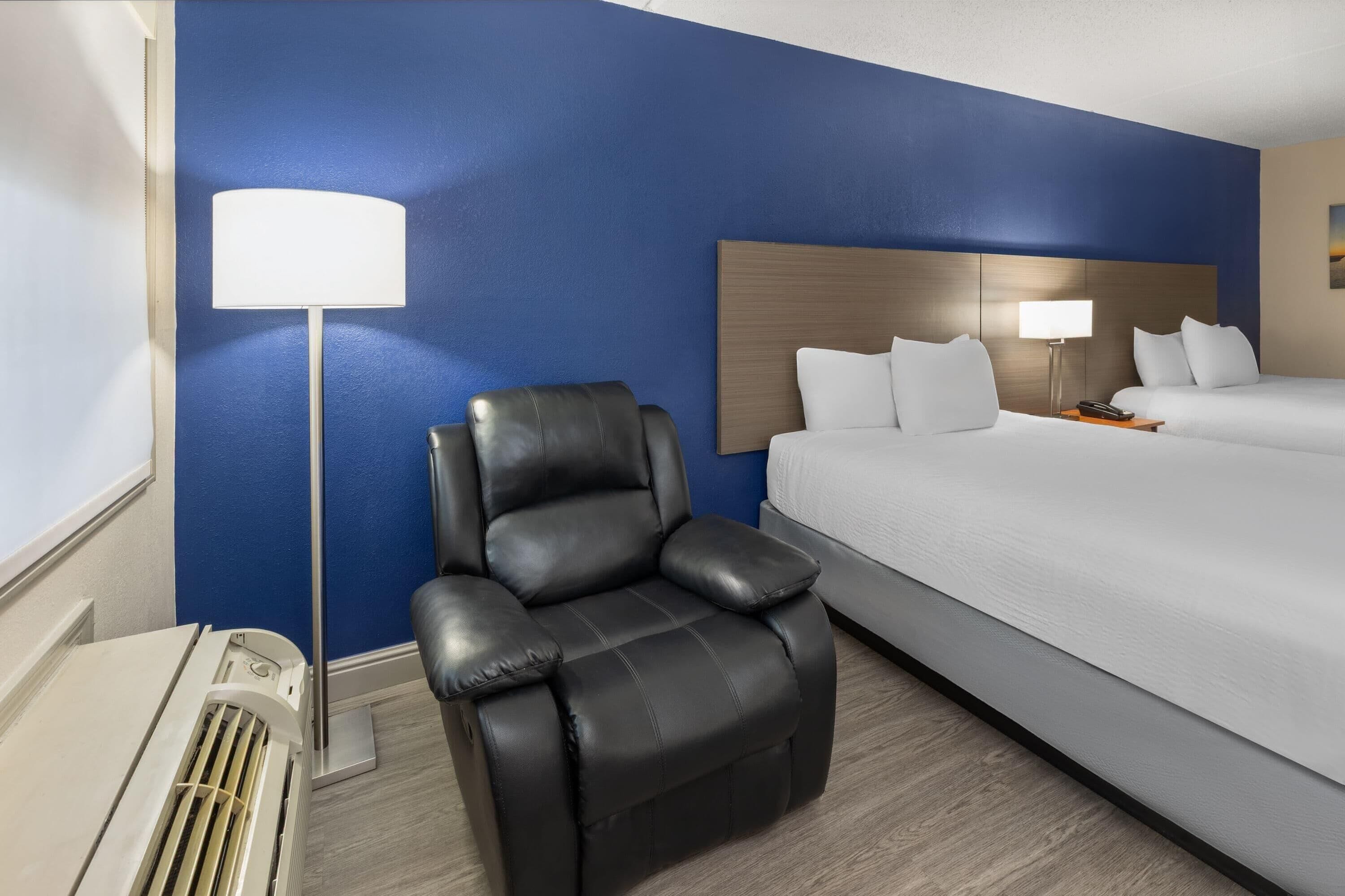 Una habitación de hotel con una cama, un sillón de cuero negro, una lámpara de pie y una mesita de noche.