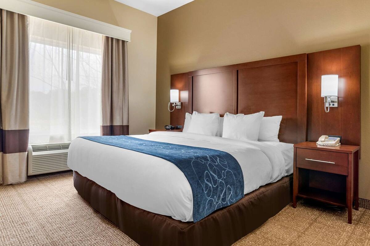 Una habitación de hotel con una cama grande, una mesita de noche con un teléfono y una ventana con cortinas.