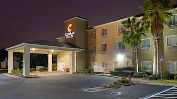 Ett Comfort Suites-hotell med en ingång som är skyddad från väder och vind, en parkeringsplats och palmer.