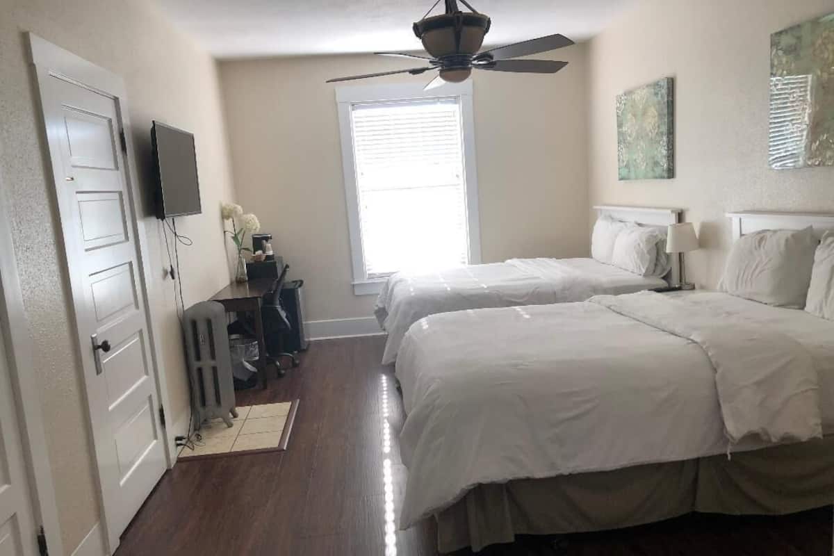 A bedroom with two beds, a ceiling fan, a TV, and a window with blinds.