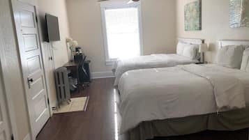 A bedroom with two beds, a ceiling fan, a TV, and a window with blinds.