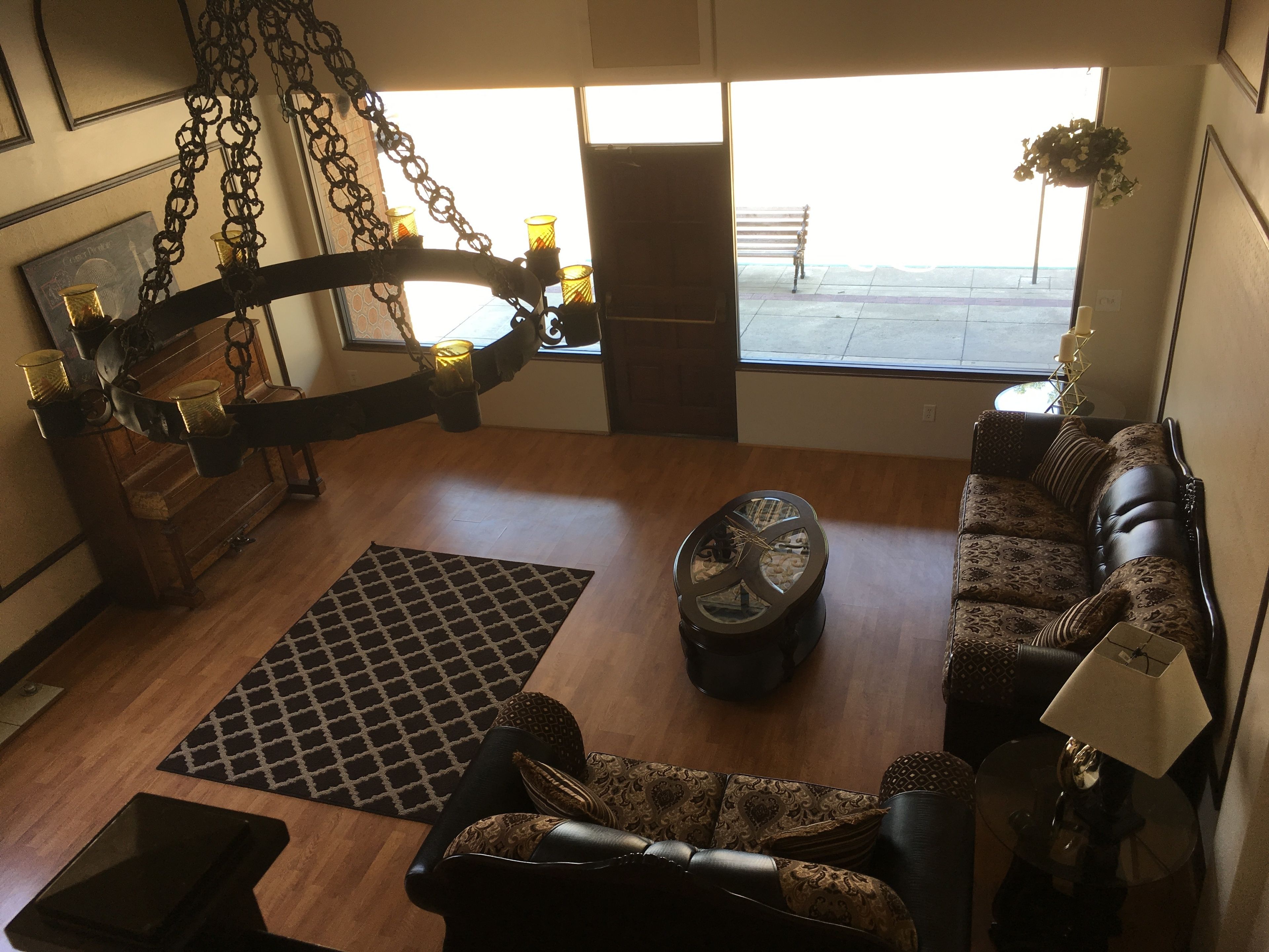 A spacious living room with a large window, a sofa, a coffee table, and a decorative chandelier.
