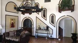 A spacious living room with a large chandelier, a sofa, a coffee table, and a staircase with decorative arches. - Hotel Burgess (Reedley)