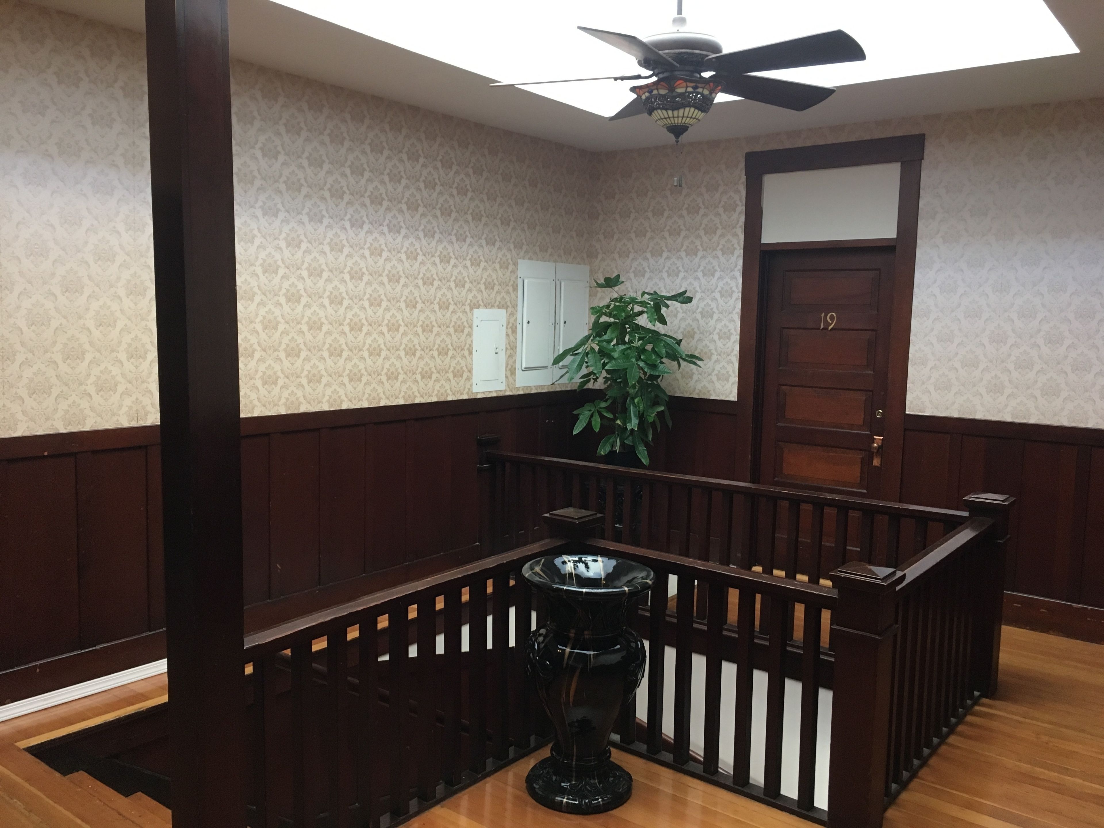 A room with a wooden staircase, a ceiling fan, a potted plant, and a door.