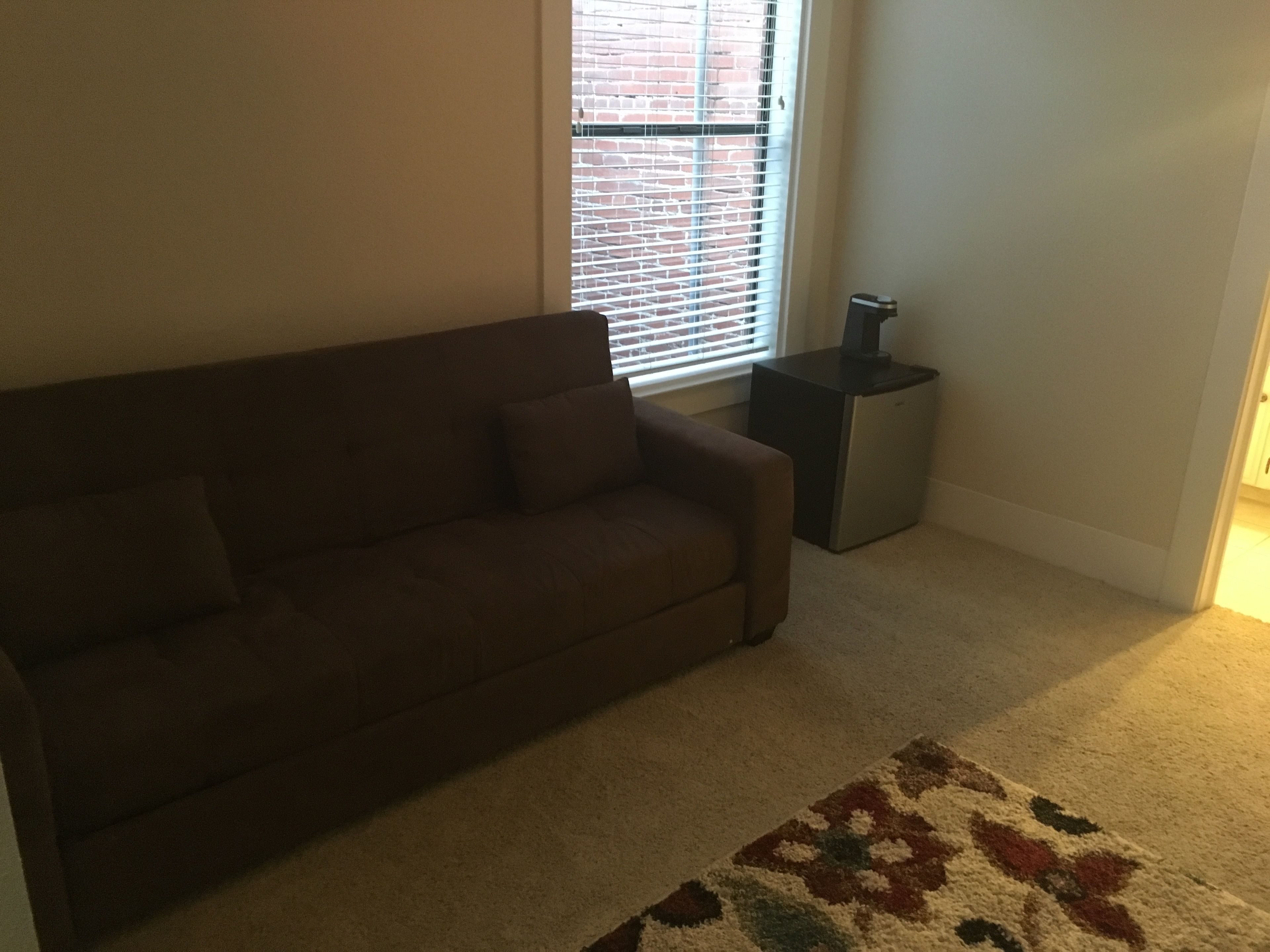 A living room with a brown sofa, a small side table, and a patterned rug.