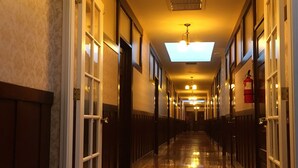 A long, narrow hallway with wooden floors and patterned wallpaper. - Hotel Burgess (Reedley)