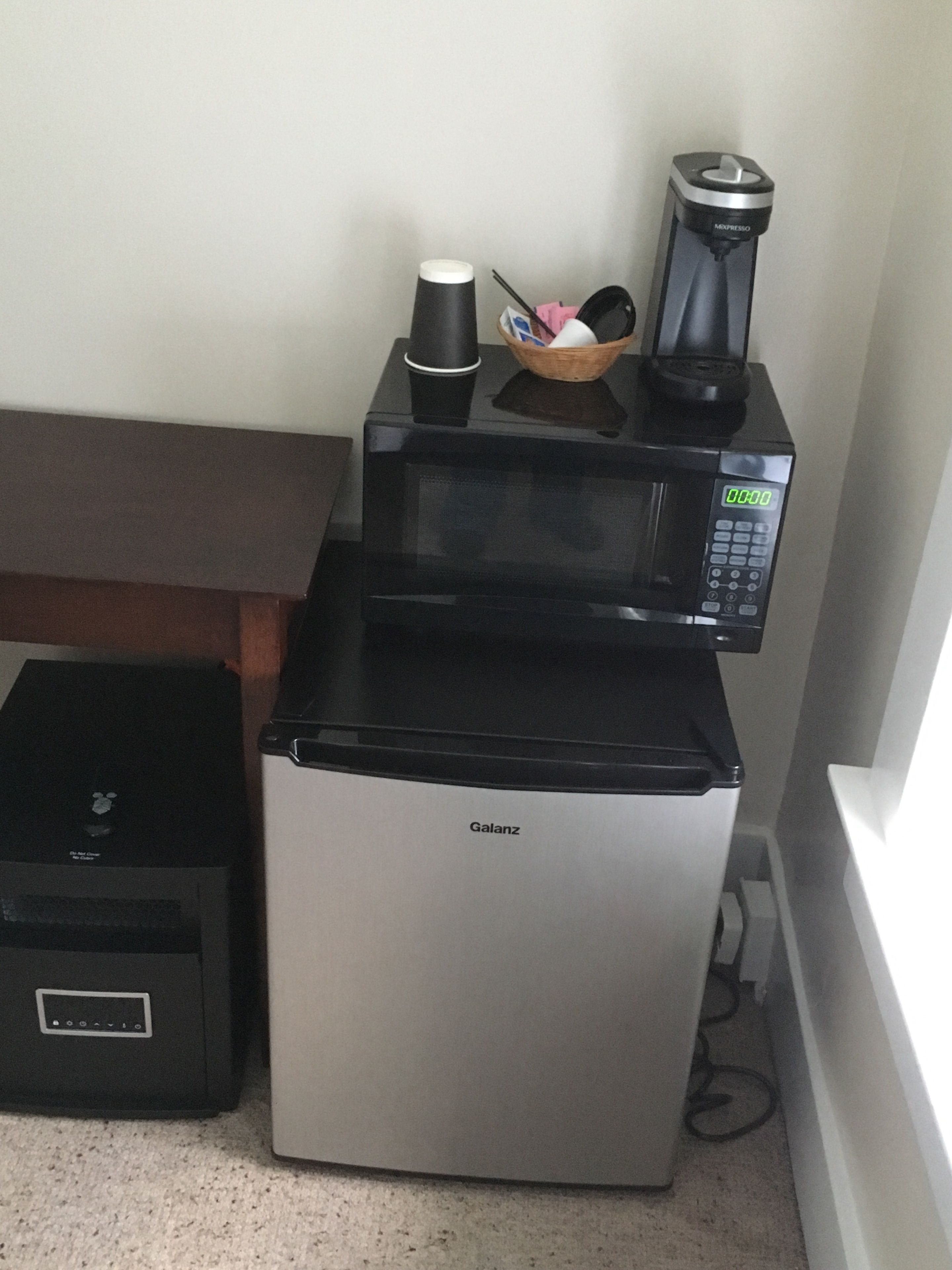 Uma cozinha compacta com cafeteira preta, micro-ondas e pequeno frigorífico.