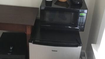 Uma cozinha compacta com cafeteira preta, micro-ondas e pequeno frigorífico.