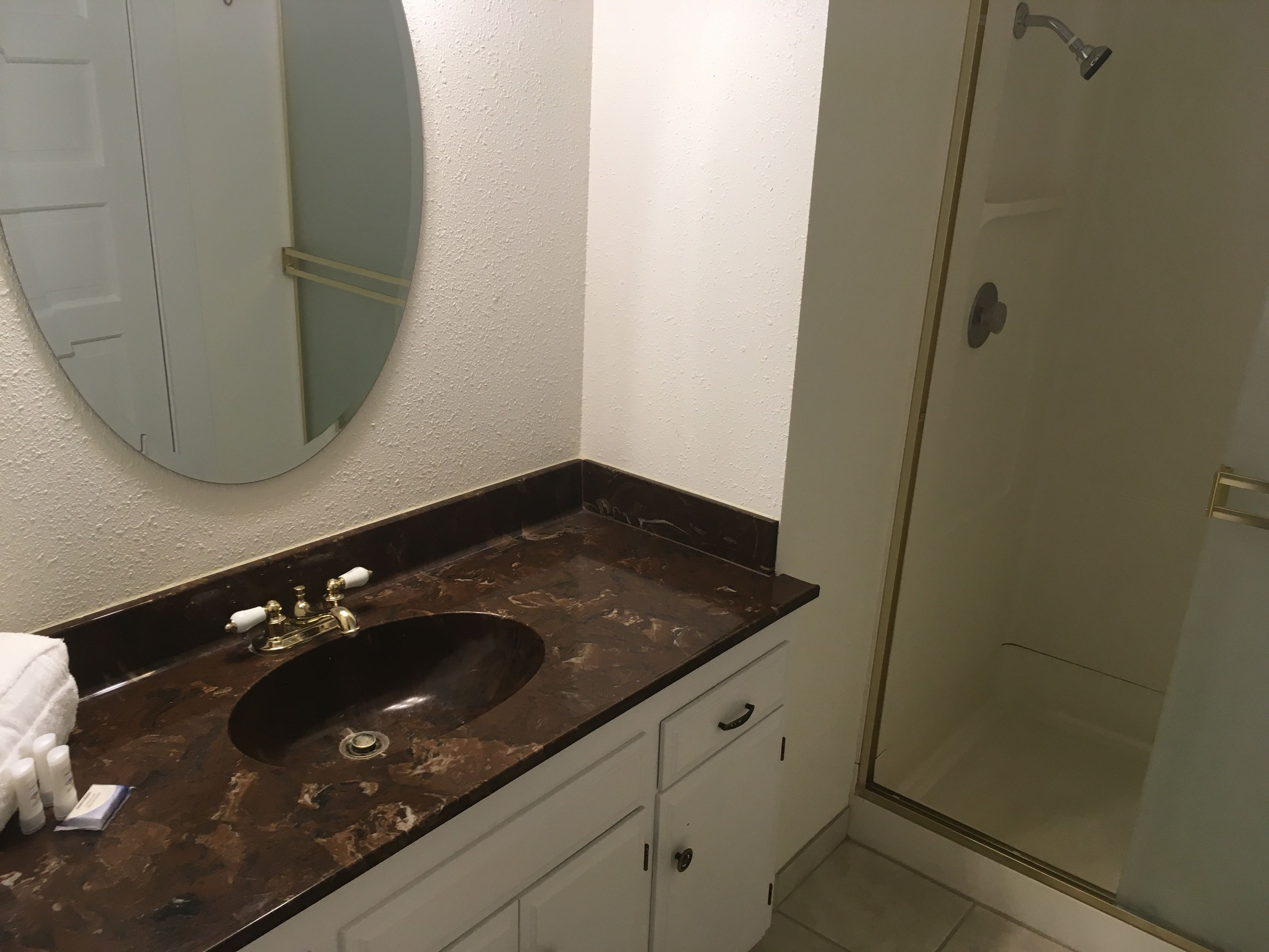 Un baño con lavamanos de mármol oscuro, un espejo y una ducha con cerramiento de vidrio.
