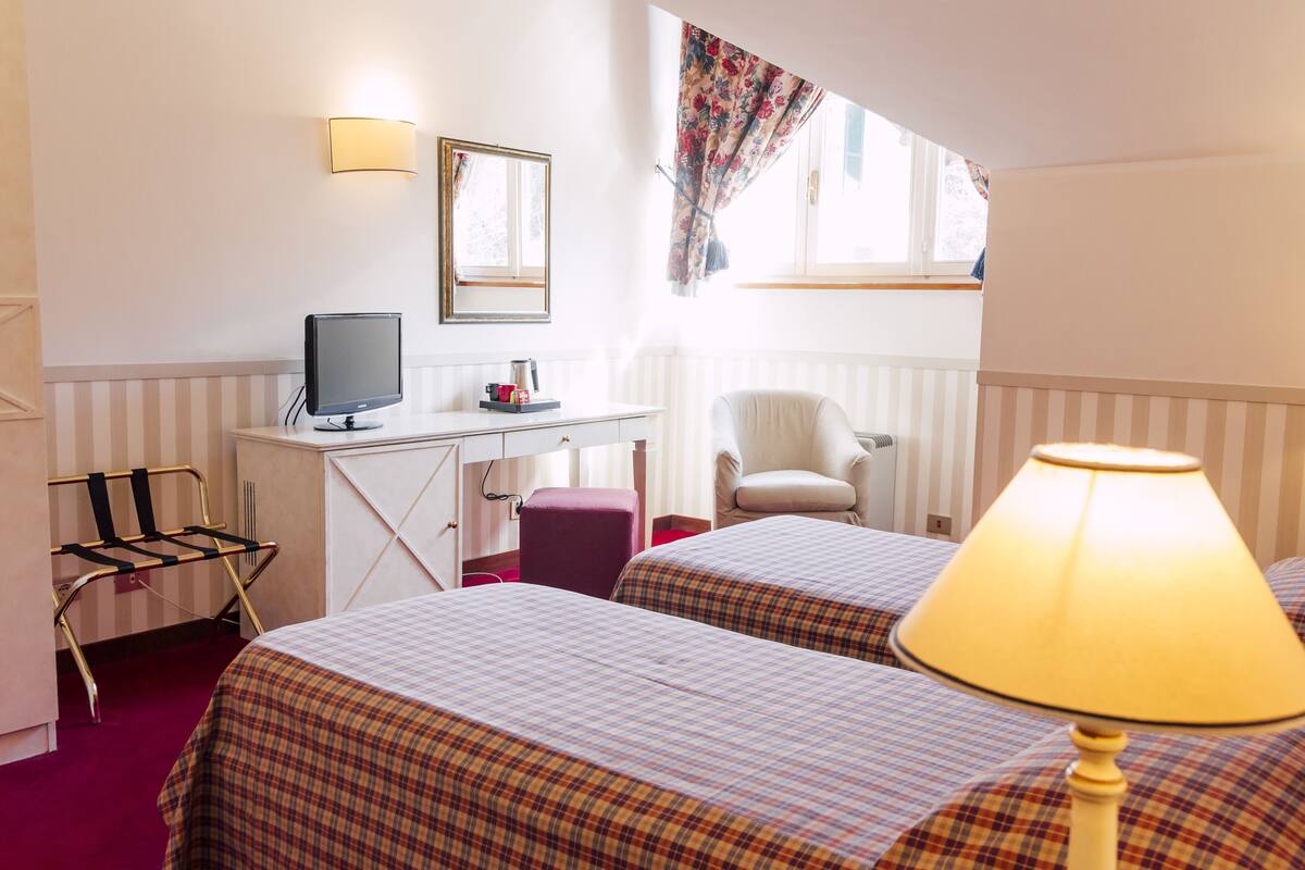 A hotel room with two beds, a desk with a computer, a chair, and a lamp.
