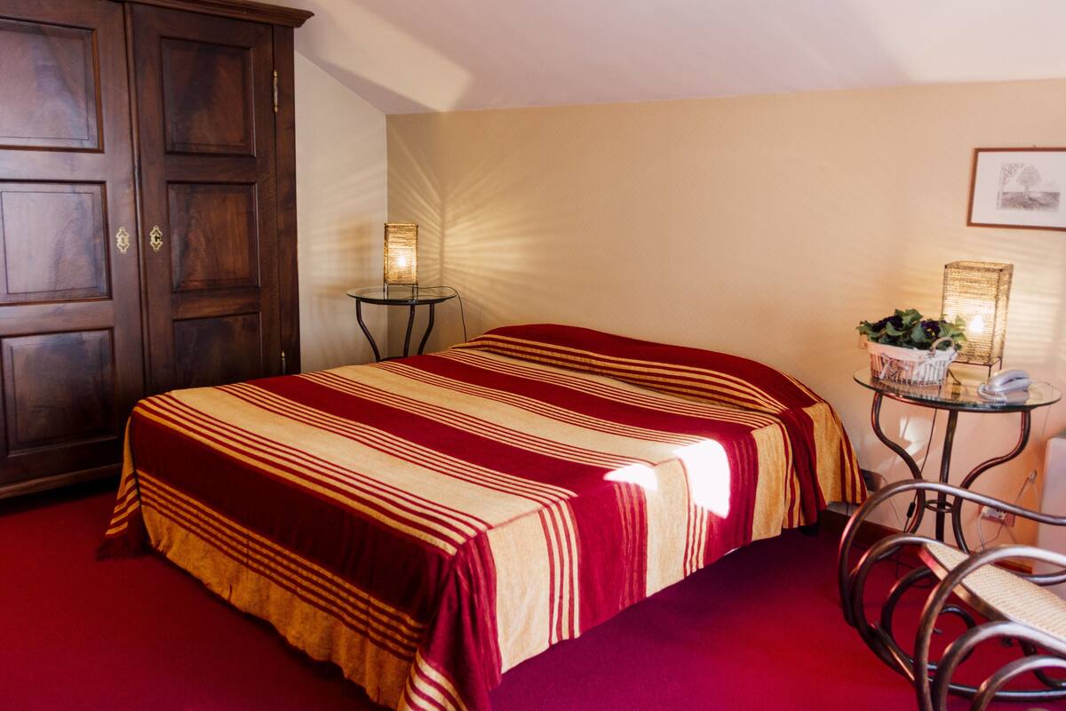 A hotel room with a large bed, a small table with a lamp, a chair, and a cabinet.