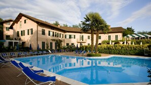 Una piscina con sillas de descanso, una palmera y un edificio con varias ventanas y balcones.