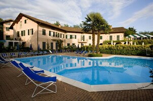 Piscina com espreguiçadeiras, uma palmeira e um edifício com várias janelas e varandas.
