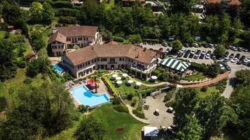 Vista aérea de um edifício grande e com vários andares, com piscina, área de estar ao ar livre e estacionamento.