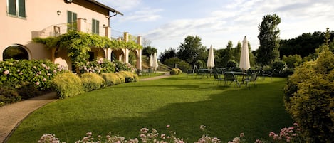 Un jardín bien cuidado con un sendero pavimentado, setos podados y una zona de estar exterior con sombrillas.
