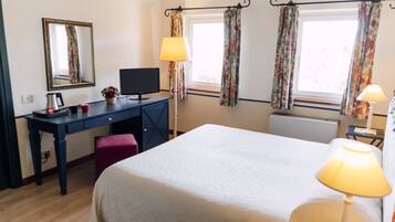Habitación de hotel con cama, escritorio, silla, lámpara y ventana con cortinas.