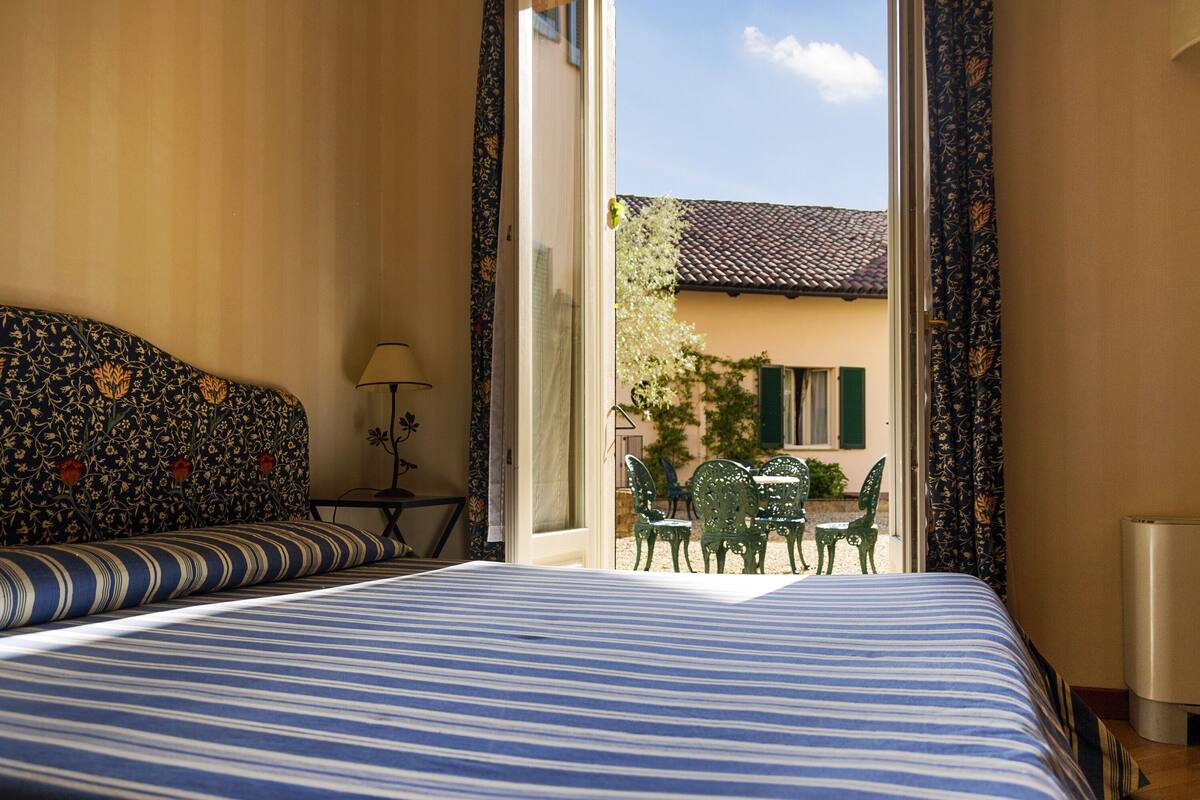A hotel room with a bed, a small table with chairs, and a view of the outside.
