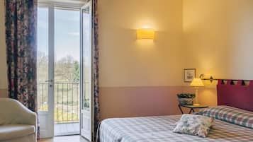 Un dormitorio con una cama, una silla, una mesita de noche con lámpara y una ventana con cortinas.