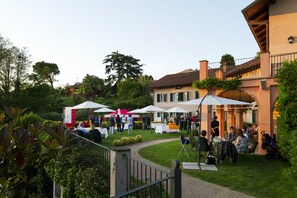 An outdoor event with tables and umbrellas, surrounded by greenery and a building with a balcony. - Hostellerie du Golf (Pecetto Torinese)