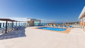 Zona de piscina en la azotea con sillones y una vista despejada del mar.