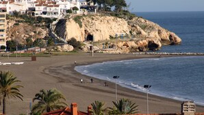 Un pueblo costero con playa, edificios sobre un acantilado y un litoral rocoso.