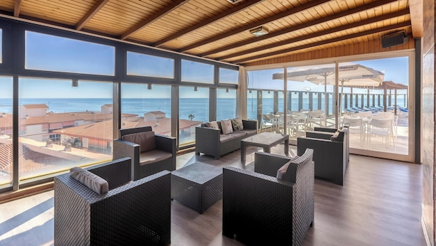 Un balcón amplio con mobiliario de mimbre, ventanas grandes y vista al mar.