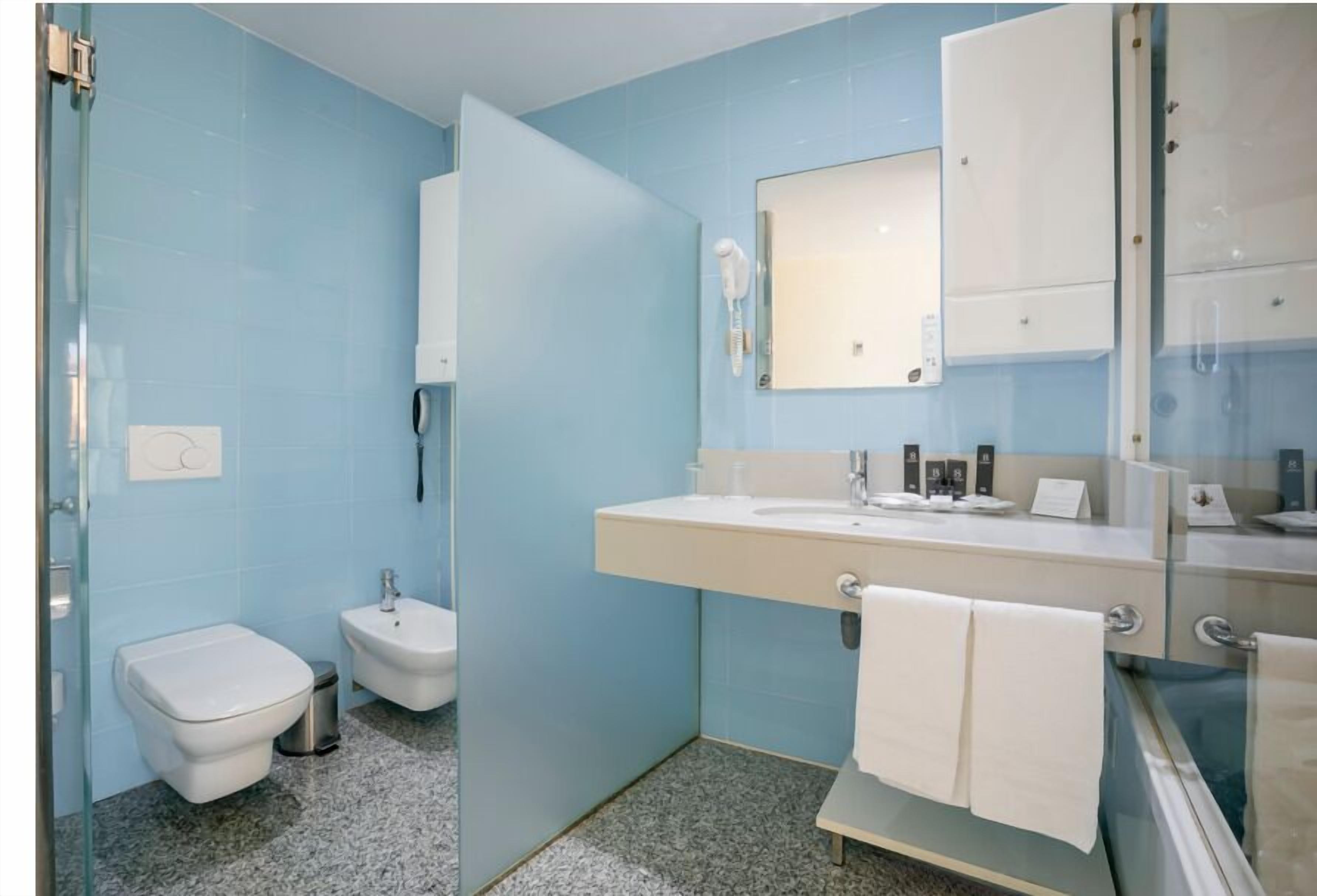 A bathroom with a glass shower enclosure, a white toilet, a bidet, and a sink with a mirror above it.