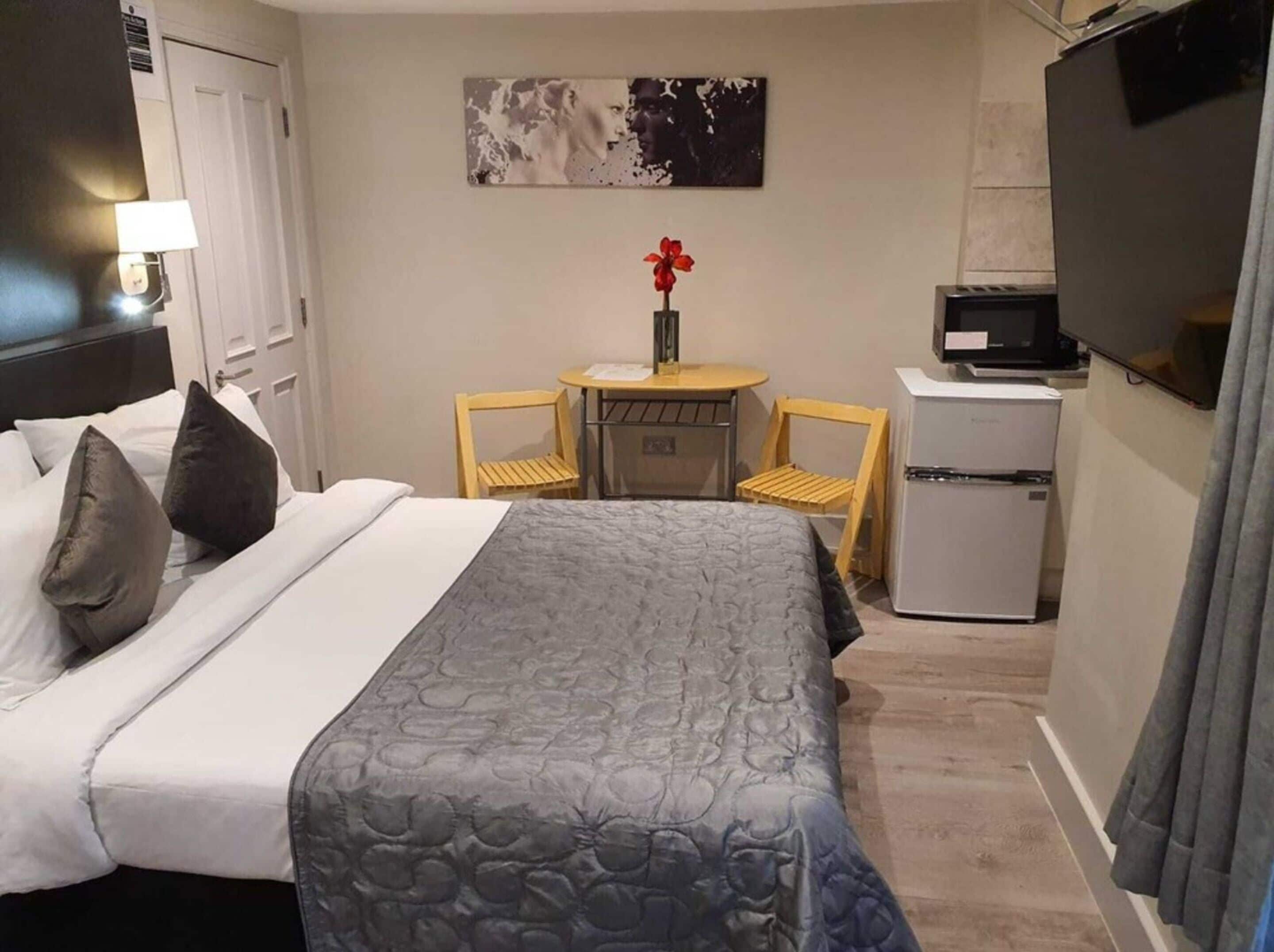 A hotel room with a bed, a desk, a chair, a TV, and a refrigerator.
