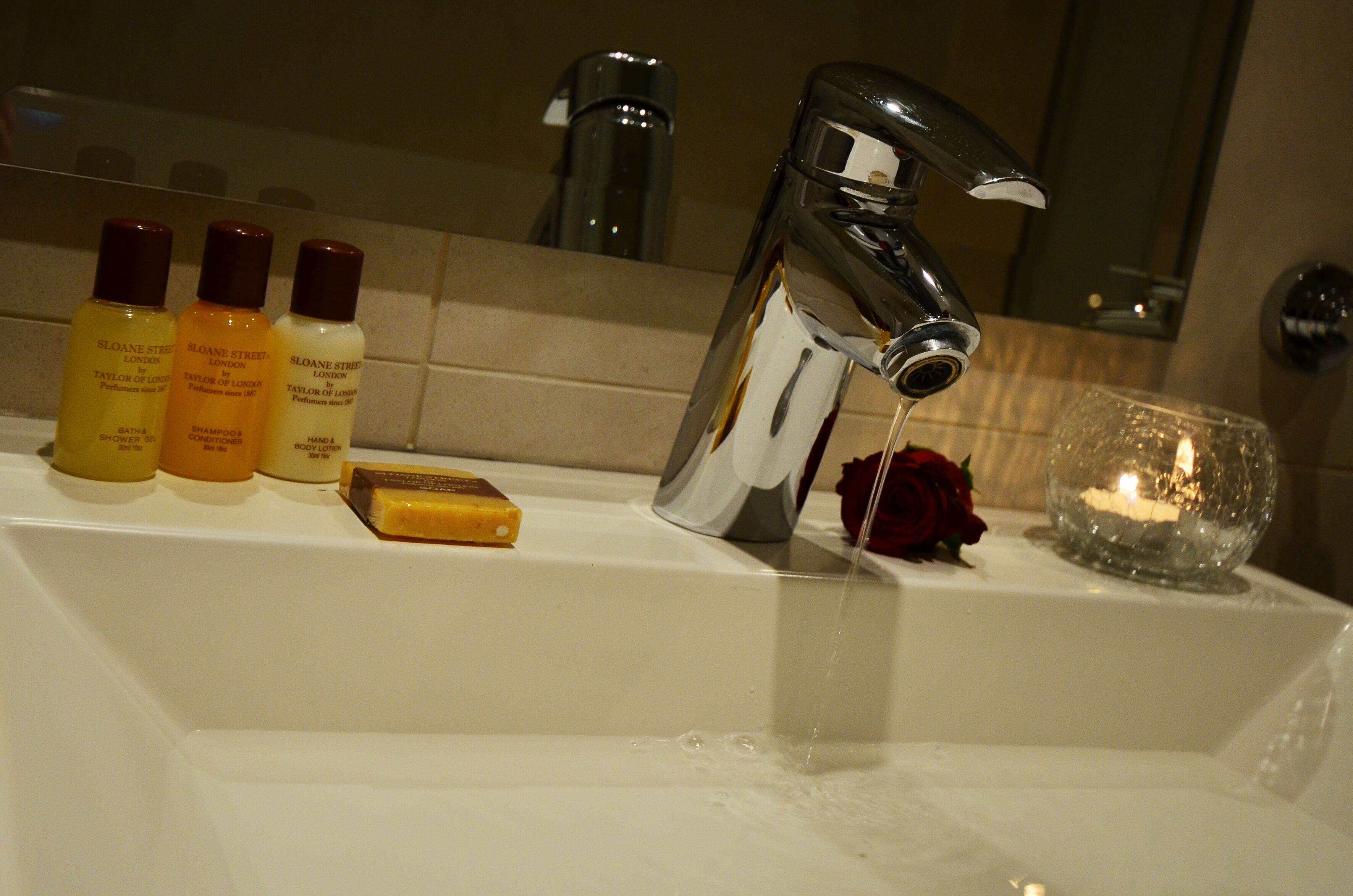 A bathroom sink with toiletries, a mirror, and a candle.