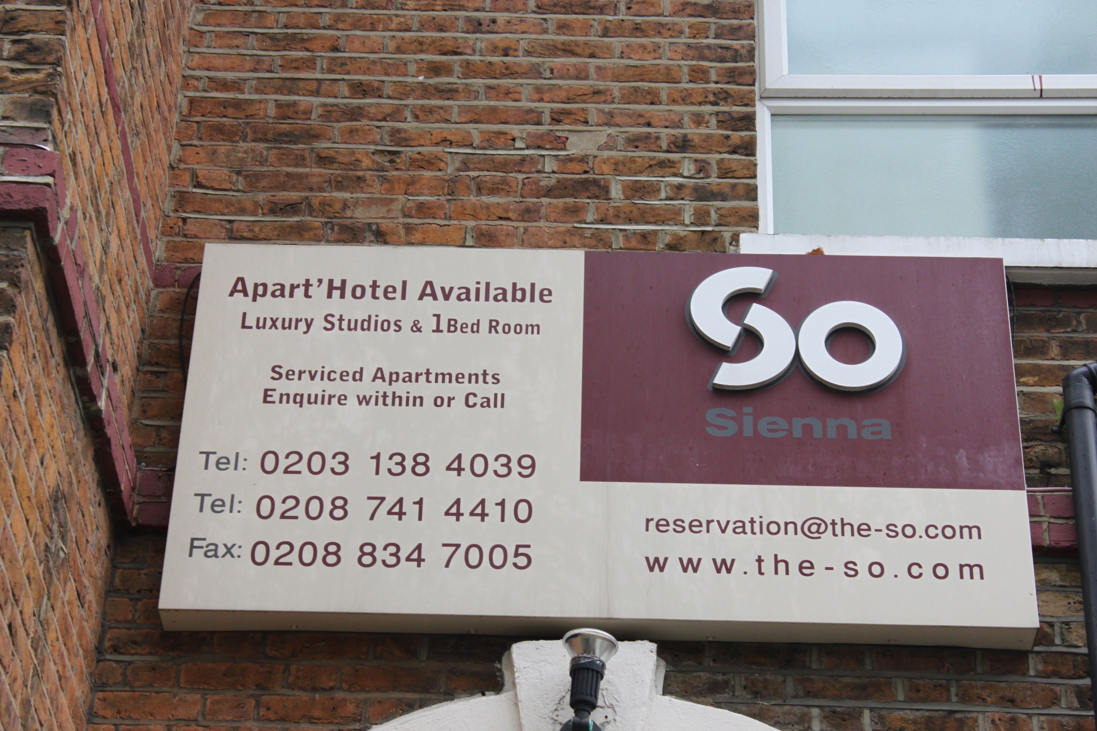 A sign for 'So Sienna' offering luxury studios and 1-bed rooms, contact details, and website information.
