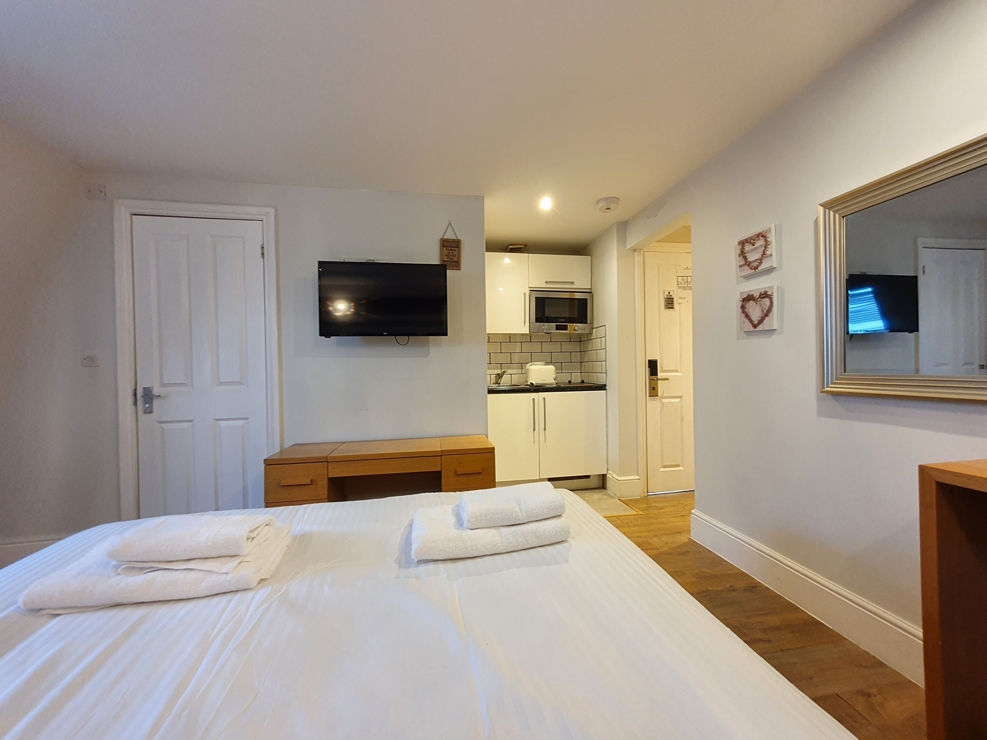 A hotel room with a bed, a desk, a TV, a microwave, and a kitchen area.