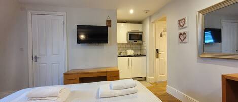 A hotel room with a bed, a desk, a TV, a microwave, and a kitchen area.