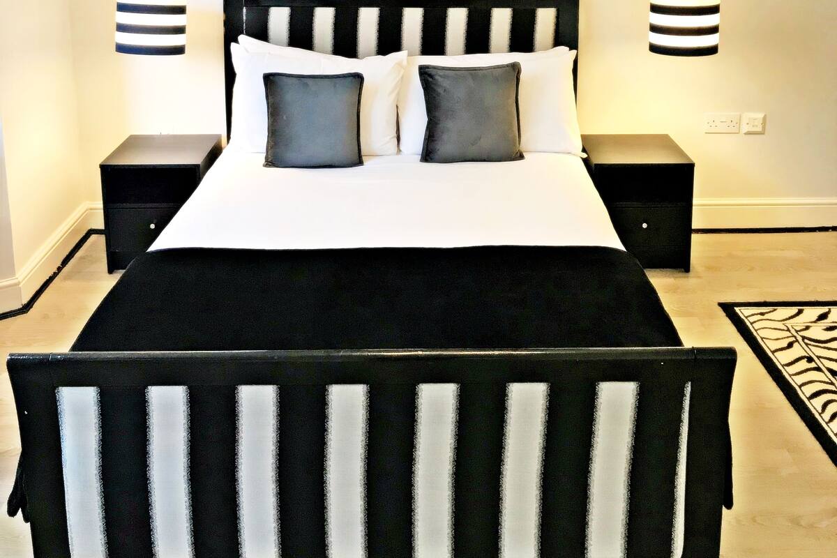 A bedroom with a black and white striped bedspread, a large framed picture of a bridge, and two bedside lamps.