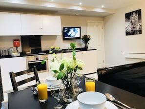 A dining area with a table set for two, a vase with flowers, and a television mounted on the wall.