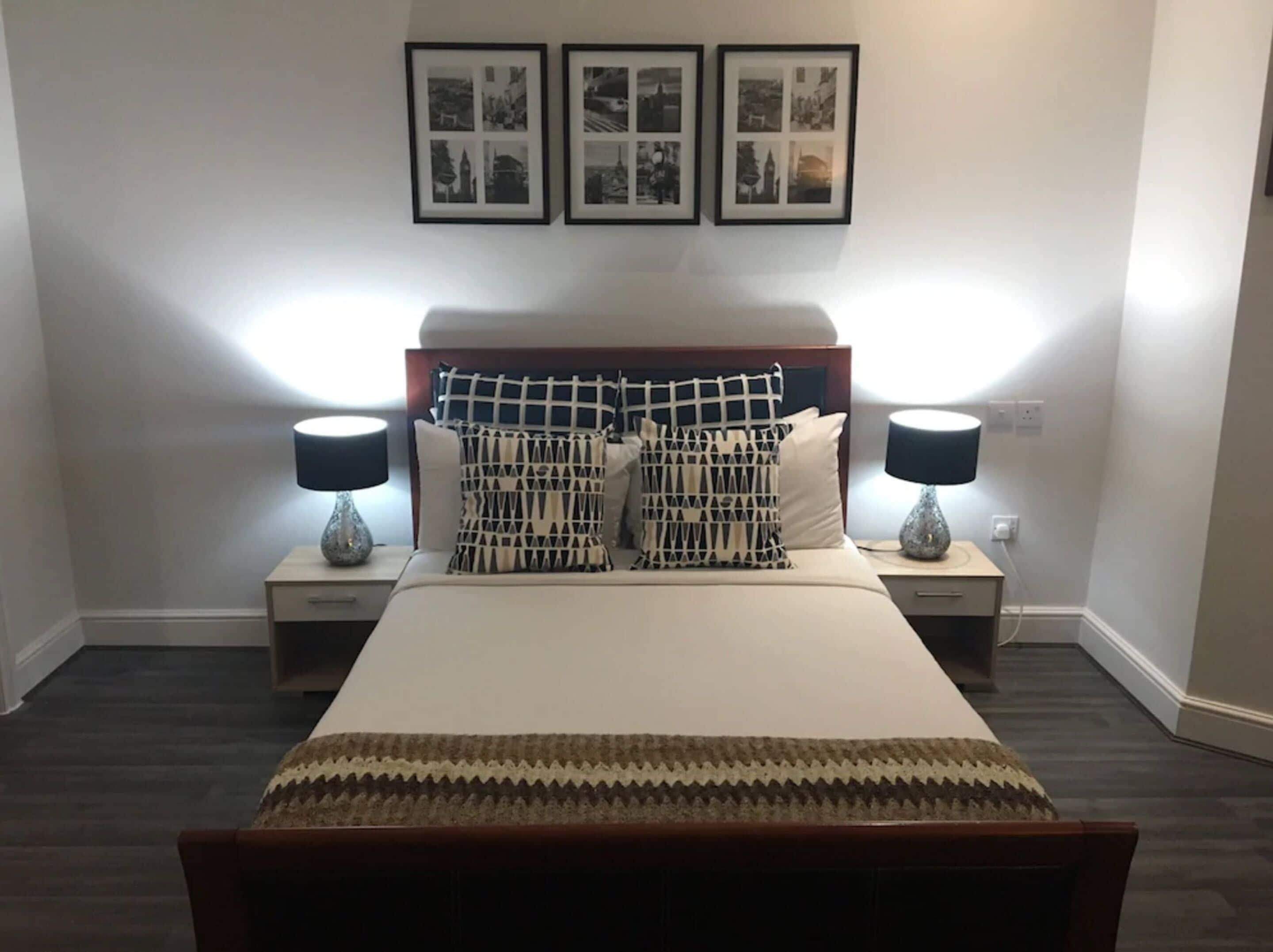 A neatly arranged bedroom with a bed, two bedside tables with lamps, a headboard, and three framed pictures on the wall.