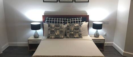 A neatly arranged bedroom with a bed, two bedside tables with lamps, a headboard, and three framed pictures on the wall.
