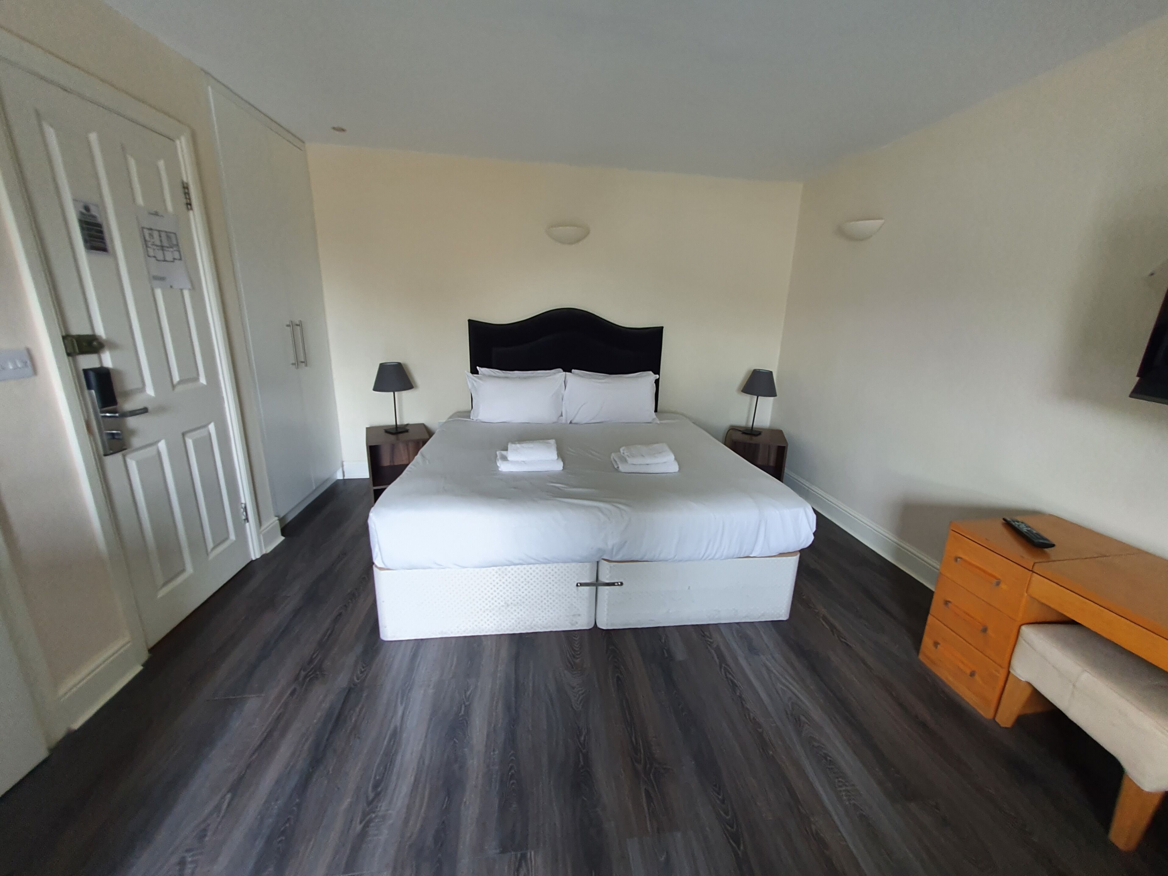 Una camera d'albergo con un letto grande, due comodini con lampade, una panca in legno e una porta con maniglia.