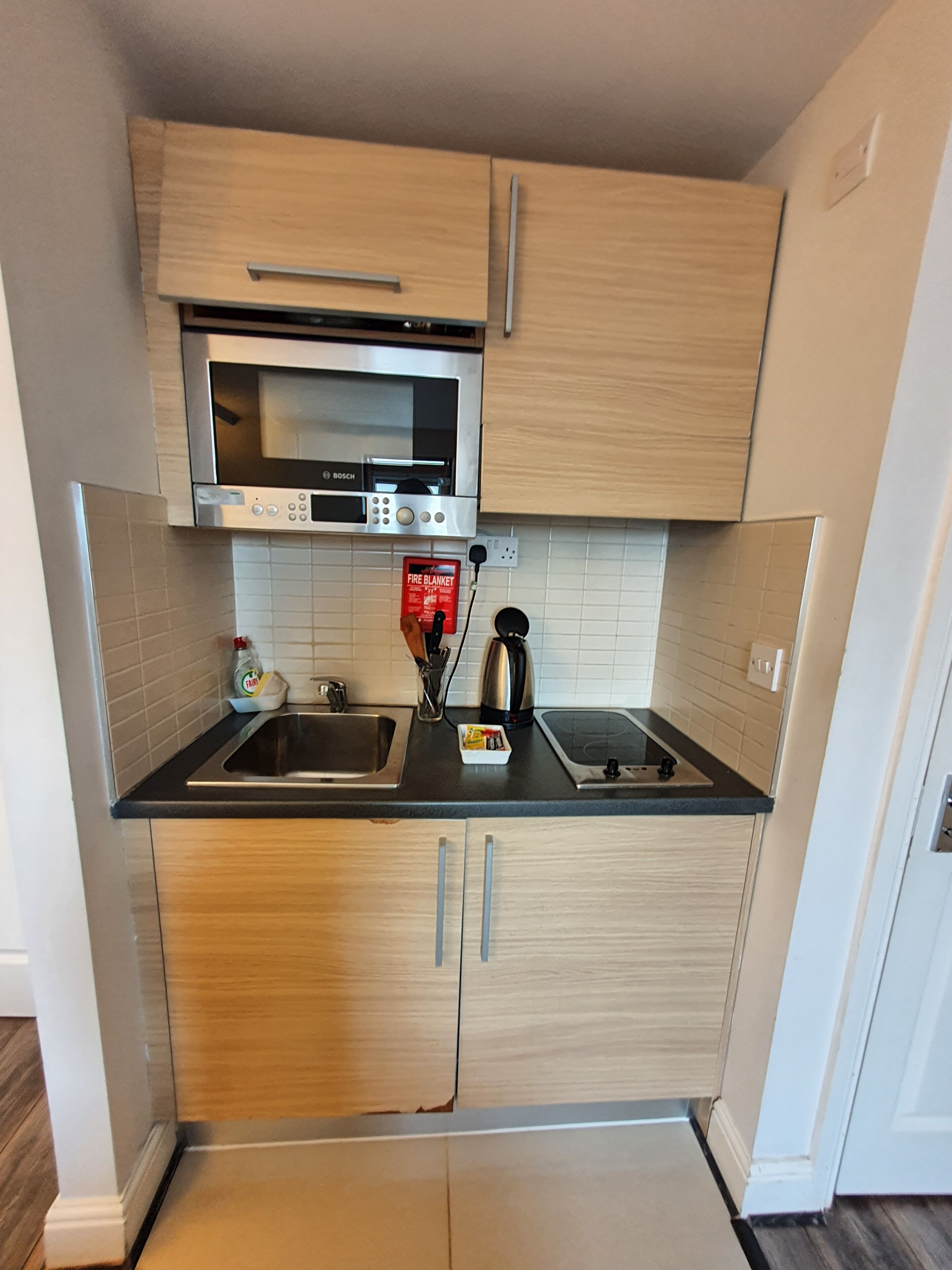 A compact kitchen with a Bosch microwave, a fire blanket, and a kettle.