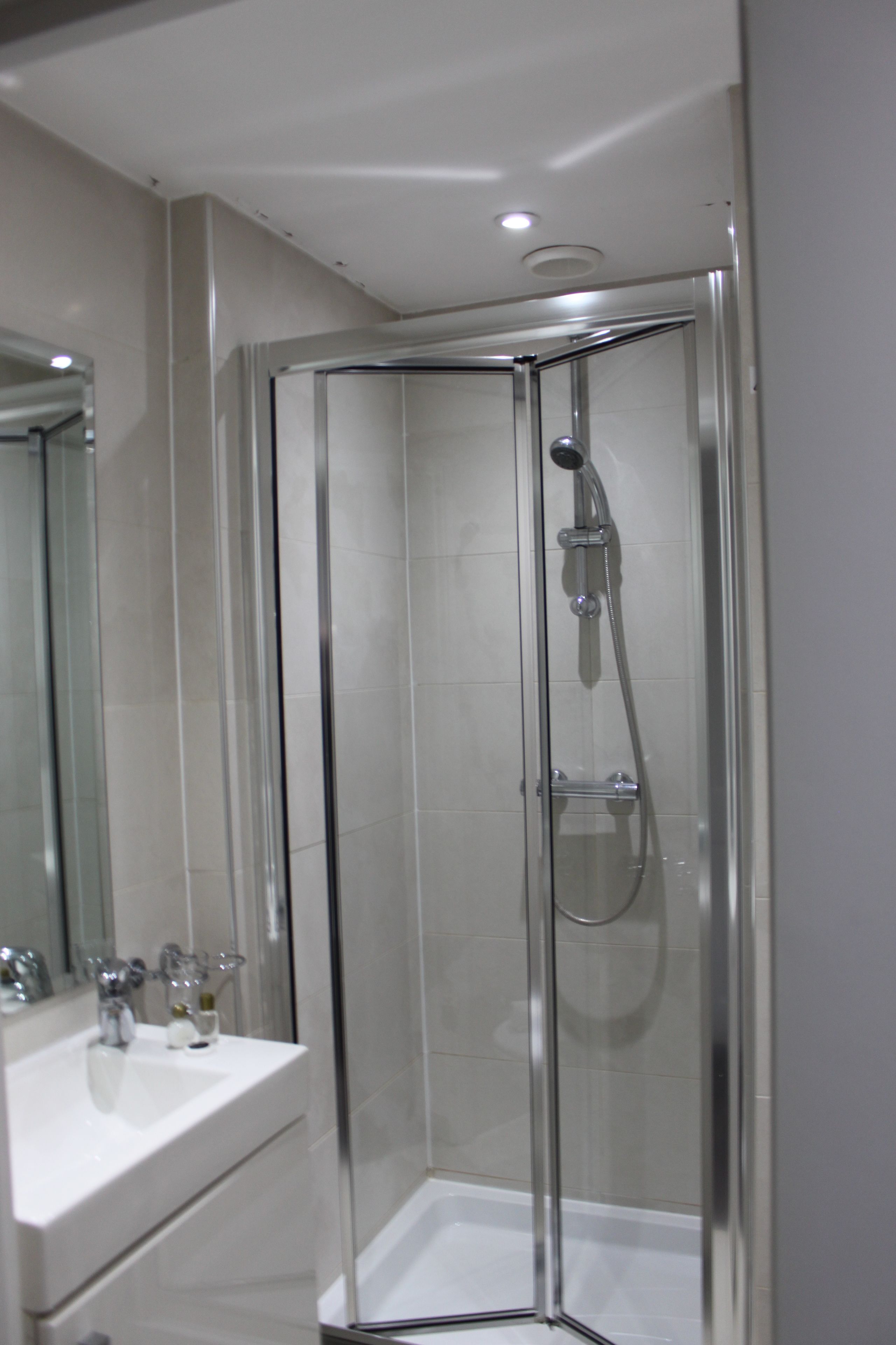 Een moderne badkamer met een douche met glazen wand, een witte wastafel en een spiegel.