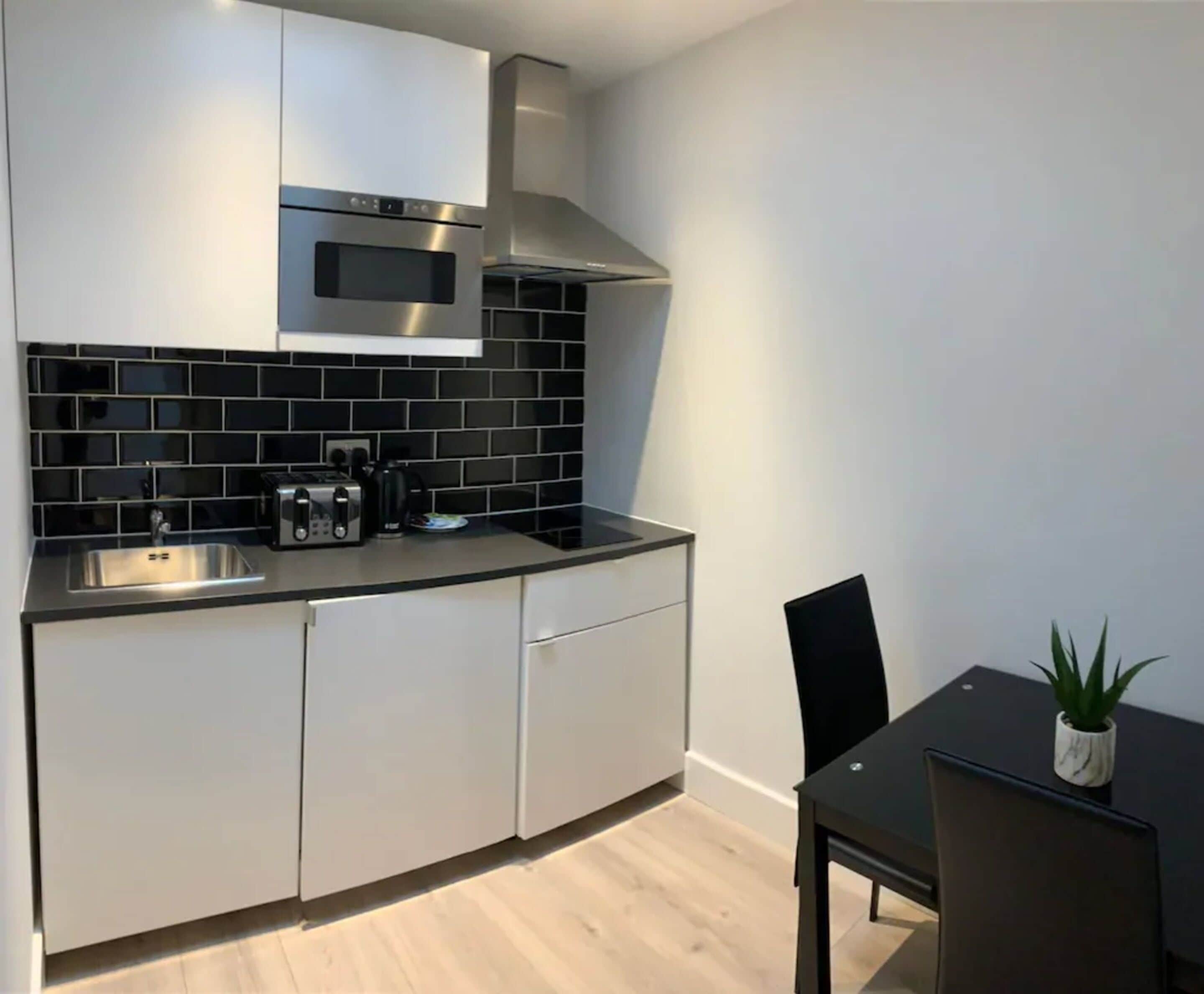 A modern kitchen with white cabinets, a stainless steel microwave, and a black tiled backsplash.