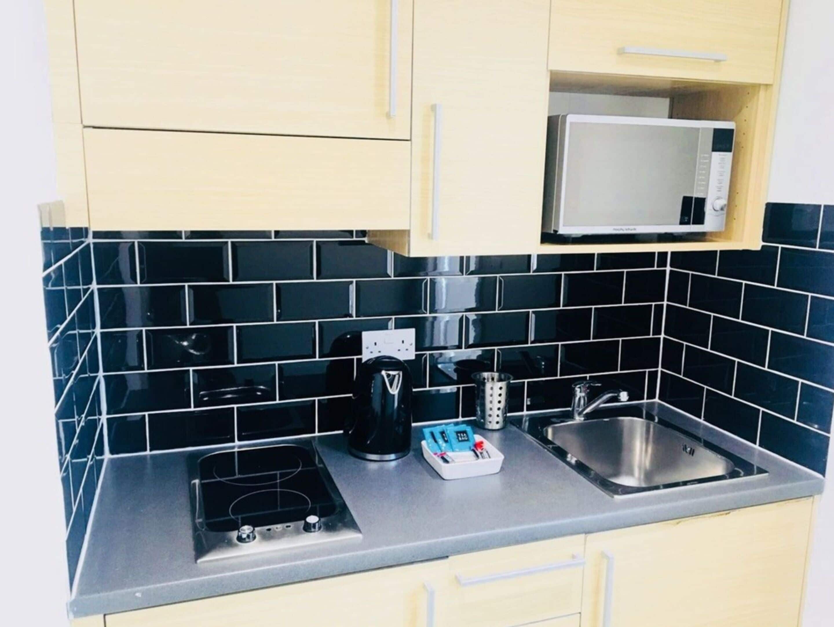 A kitchen with a black tiled backsplash, a microwave, a coffee maker, and a sink.