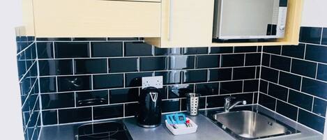 A kitchen with a black tiled backsplash, a microwave, a coffee maker, and a sink.