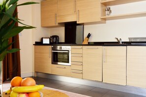 Een moderne keuken met houten kastjes, een inbouwoven en een fruitschaal op het aanrecht.