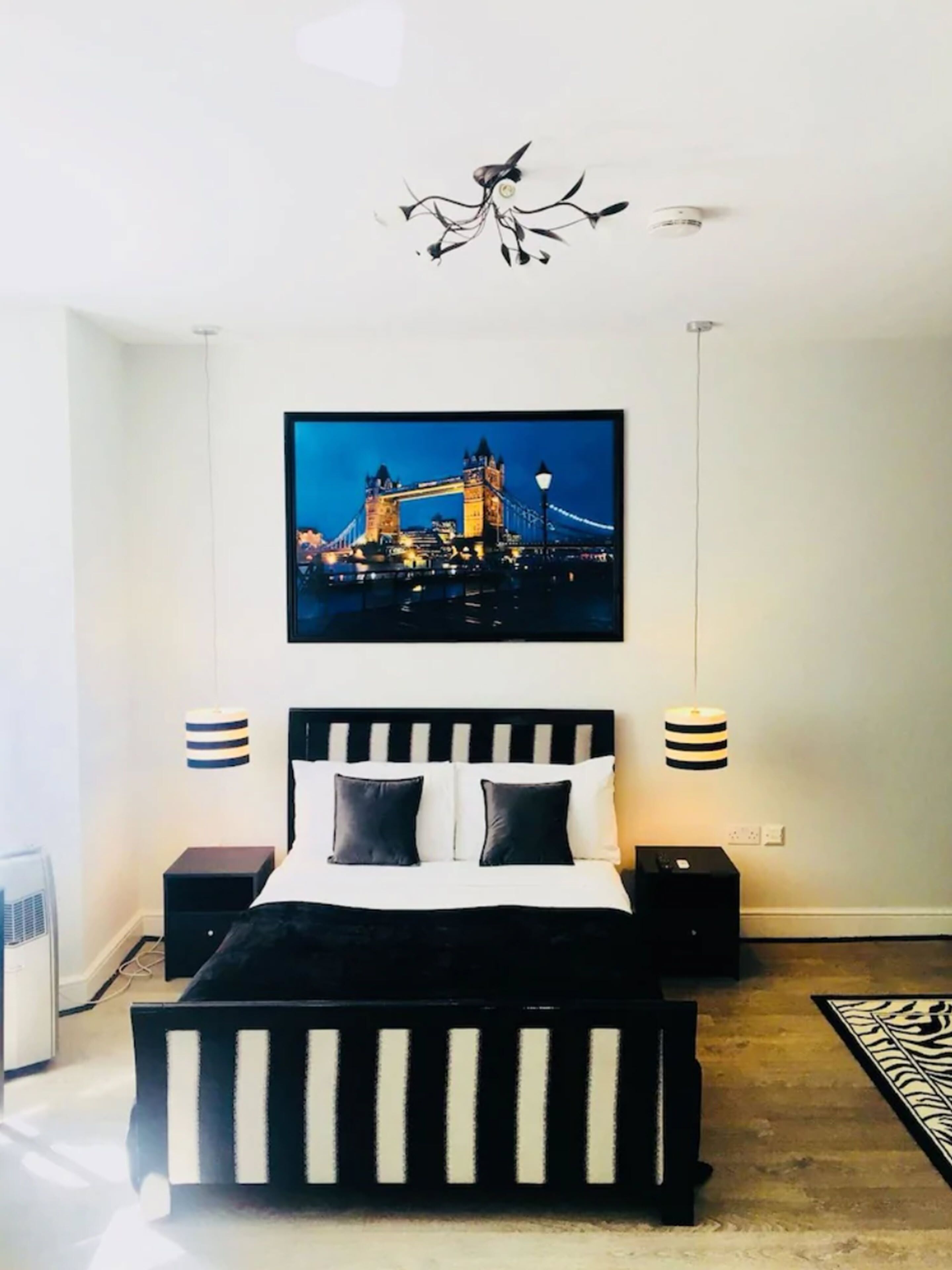 A modern bedroom with a black and white striped bed, a cityscape painting above the bed, and two bedside lamps.