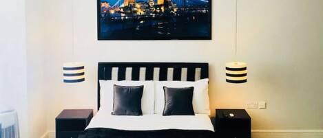 A modern bedroom with a black and white striped bed, a cityscape painting above the bed, and two bedside lamps.
