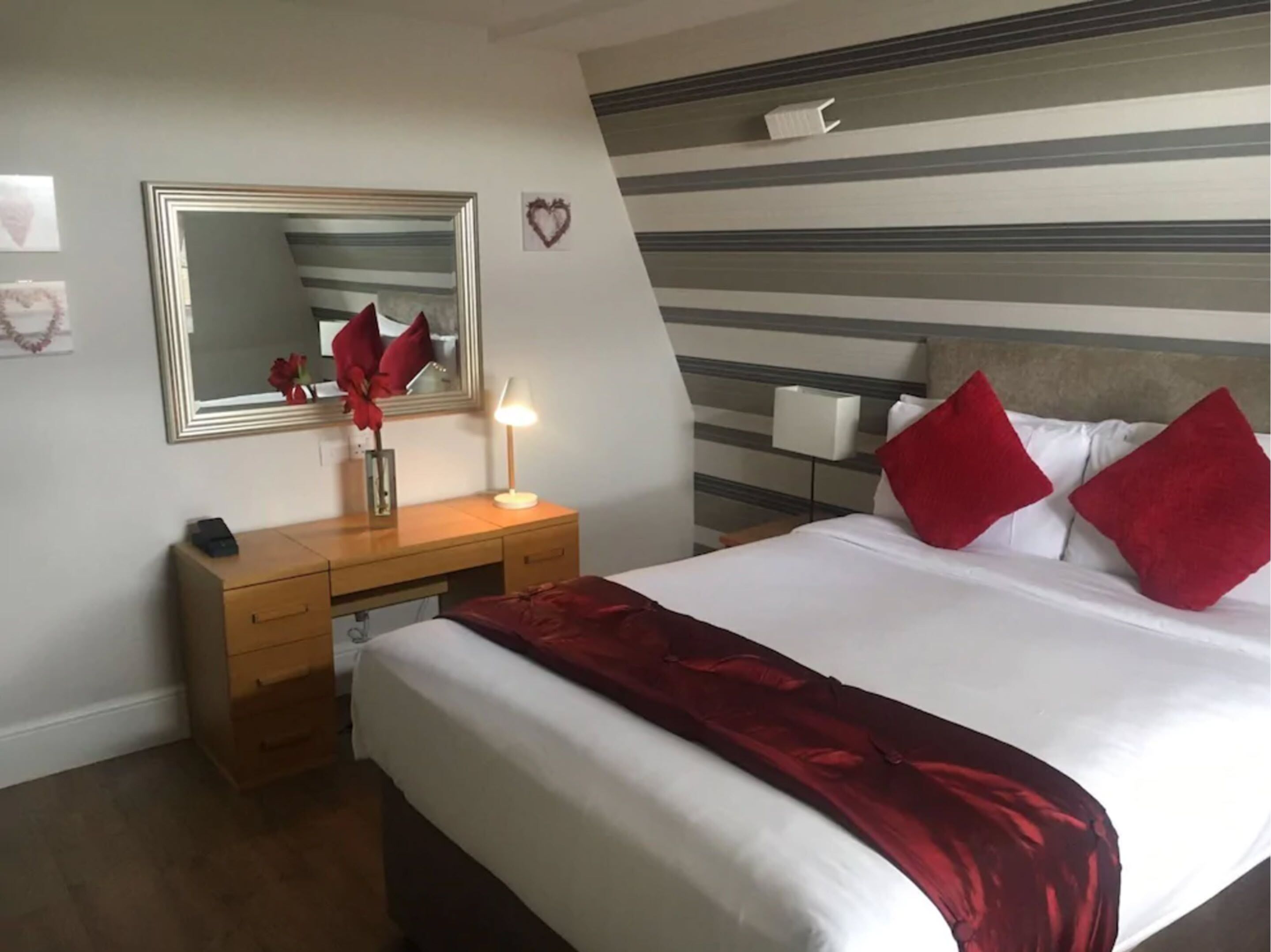 A hotel room with a bed, a bedside table, a mirror, and a dresser.